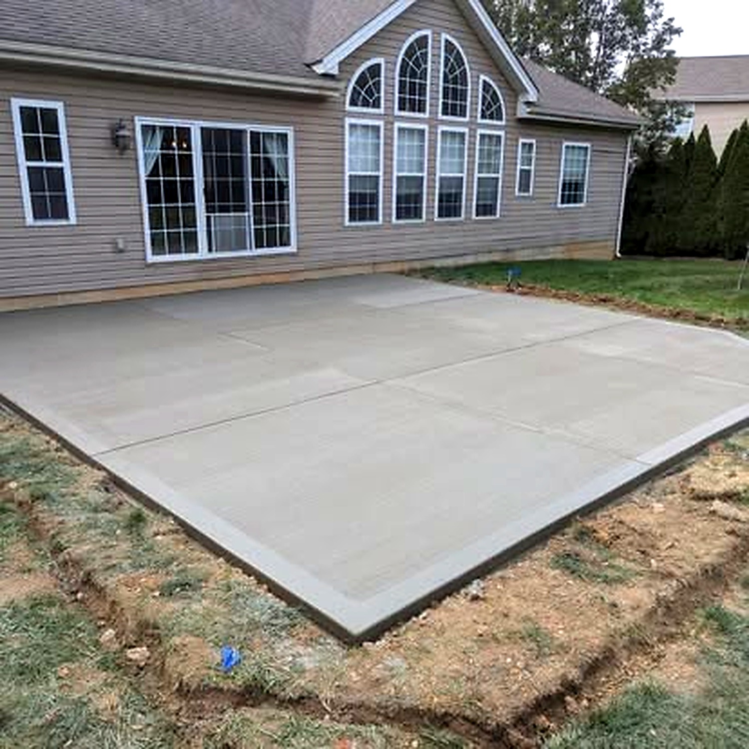 Large concrete patio installation behind tan home — True Form Concrete